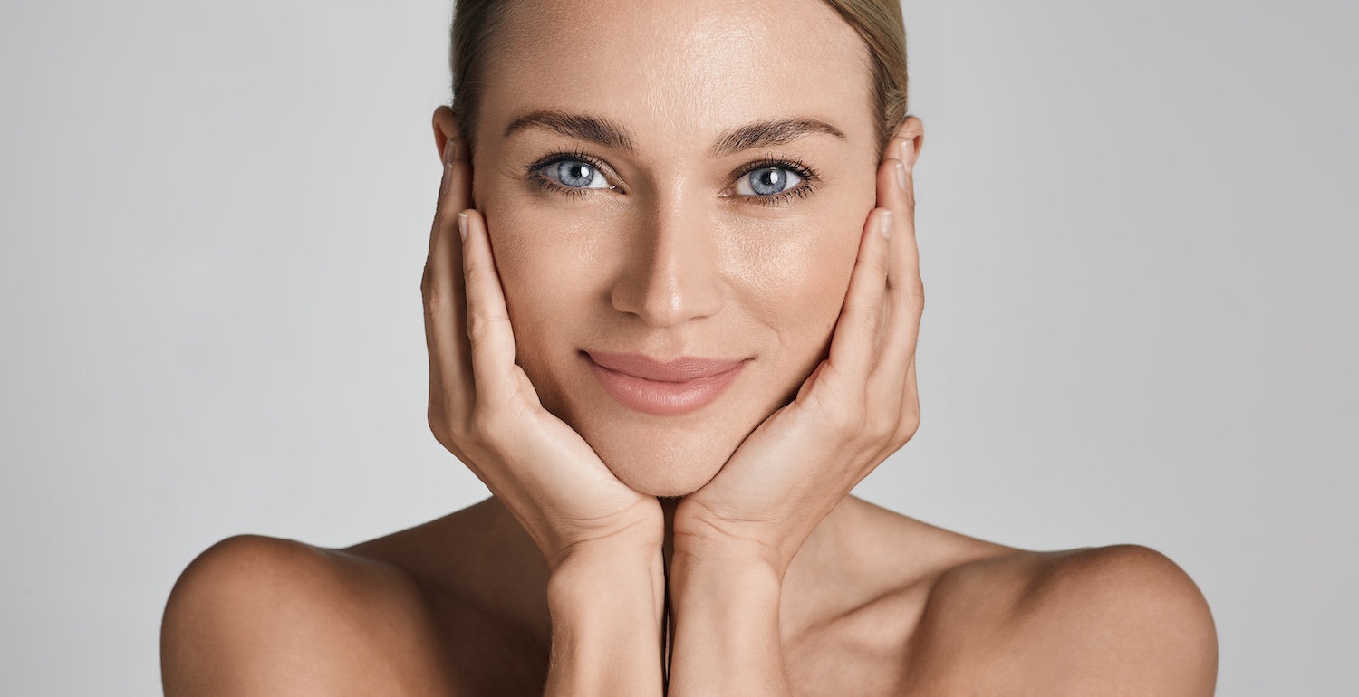 woman facing forward with hands on her cheeks and clear, even skin